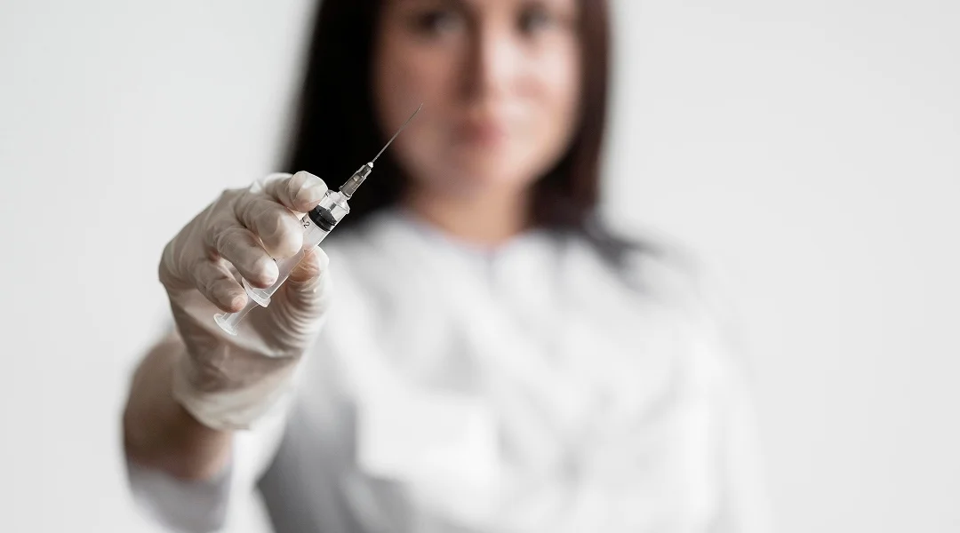 Une femme en manteau blanc tient une seringue, prête à administrer un vaccin ou un traitement médical.