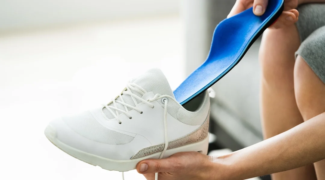 A person holds a shoe with a removable insert, demonstrating its fit and support features.